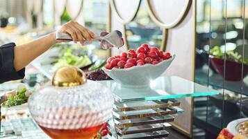 A buffet setup with a variety of food items, including a bowl of red tomatoes and a decorative glass bowl.