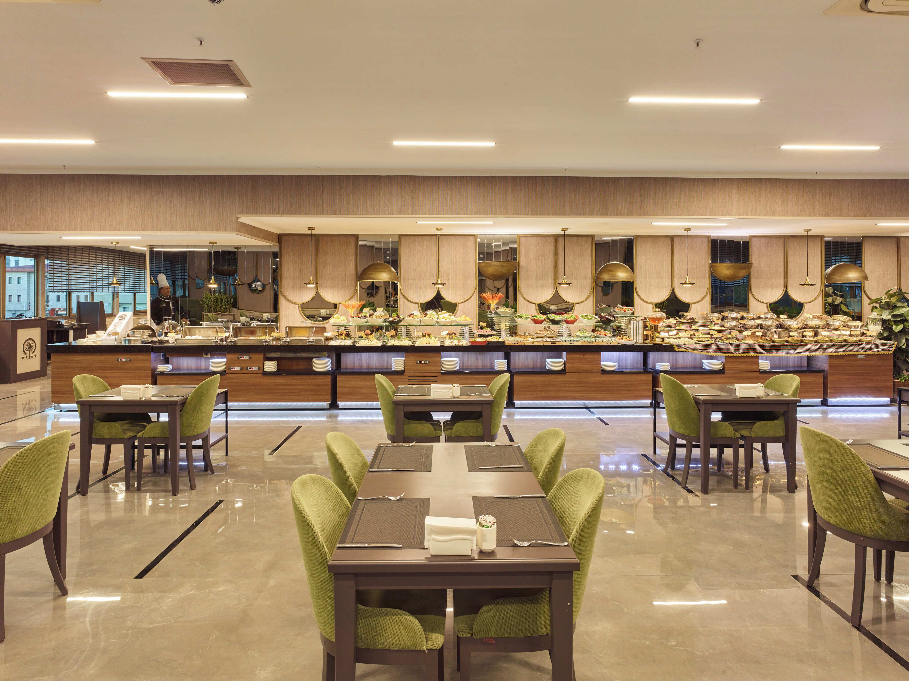 Un restaurant proposant un buffet avec de nombreuses tables et chaises, un espace central où les plats sont présentés et où l’on peut se servir, et un décor intérieur moderne.