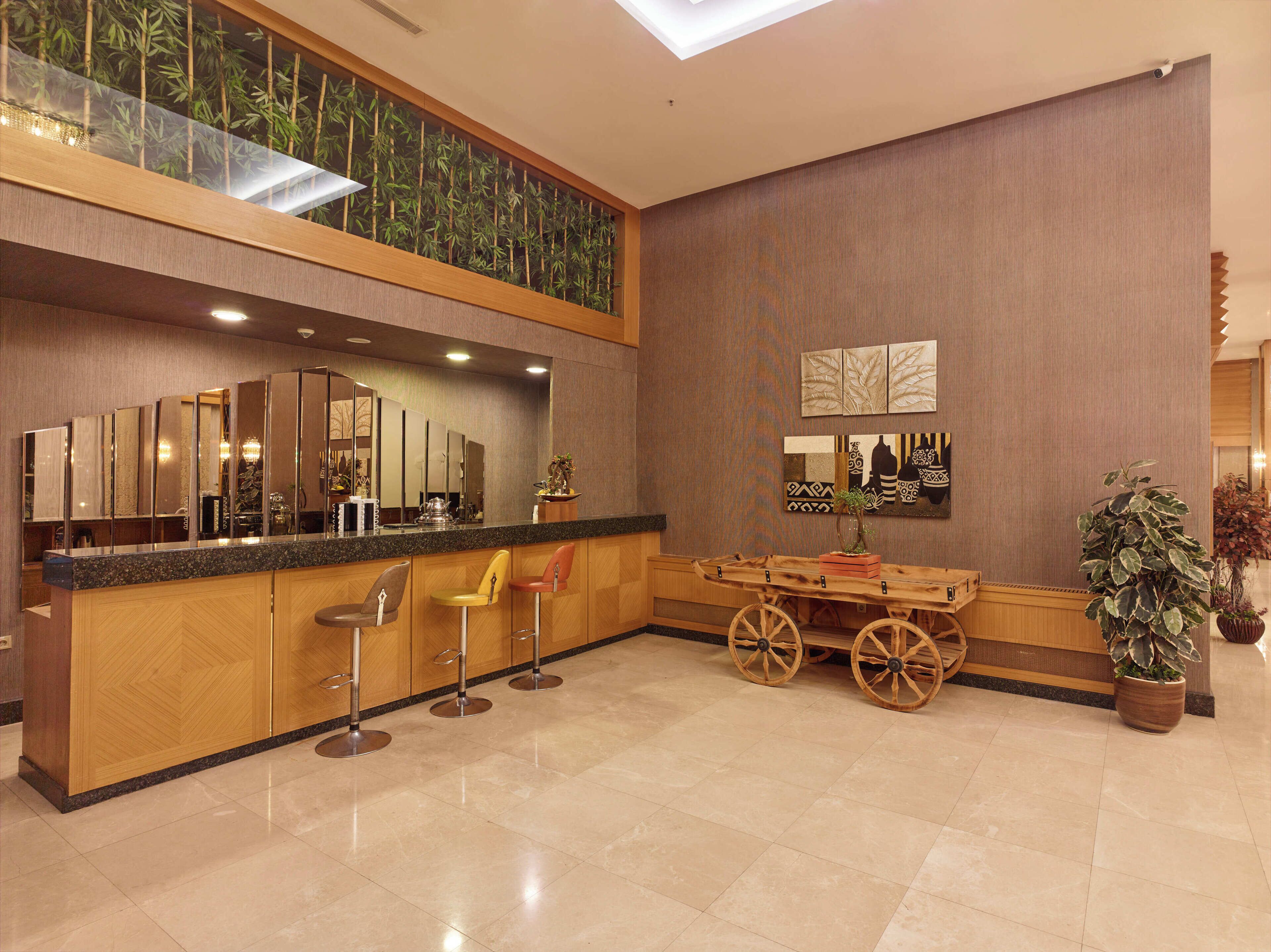 A modern hotel lobby with a high ceiling, a central bar area, and a seating arrangement with a wooden cart.