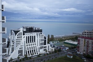 A modern building with unique architectural design, a view of the sea, and a road with vehicles.
