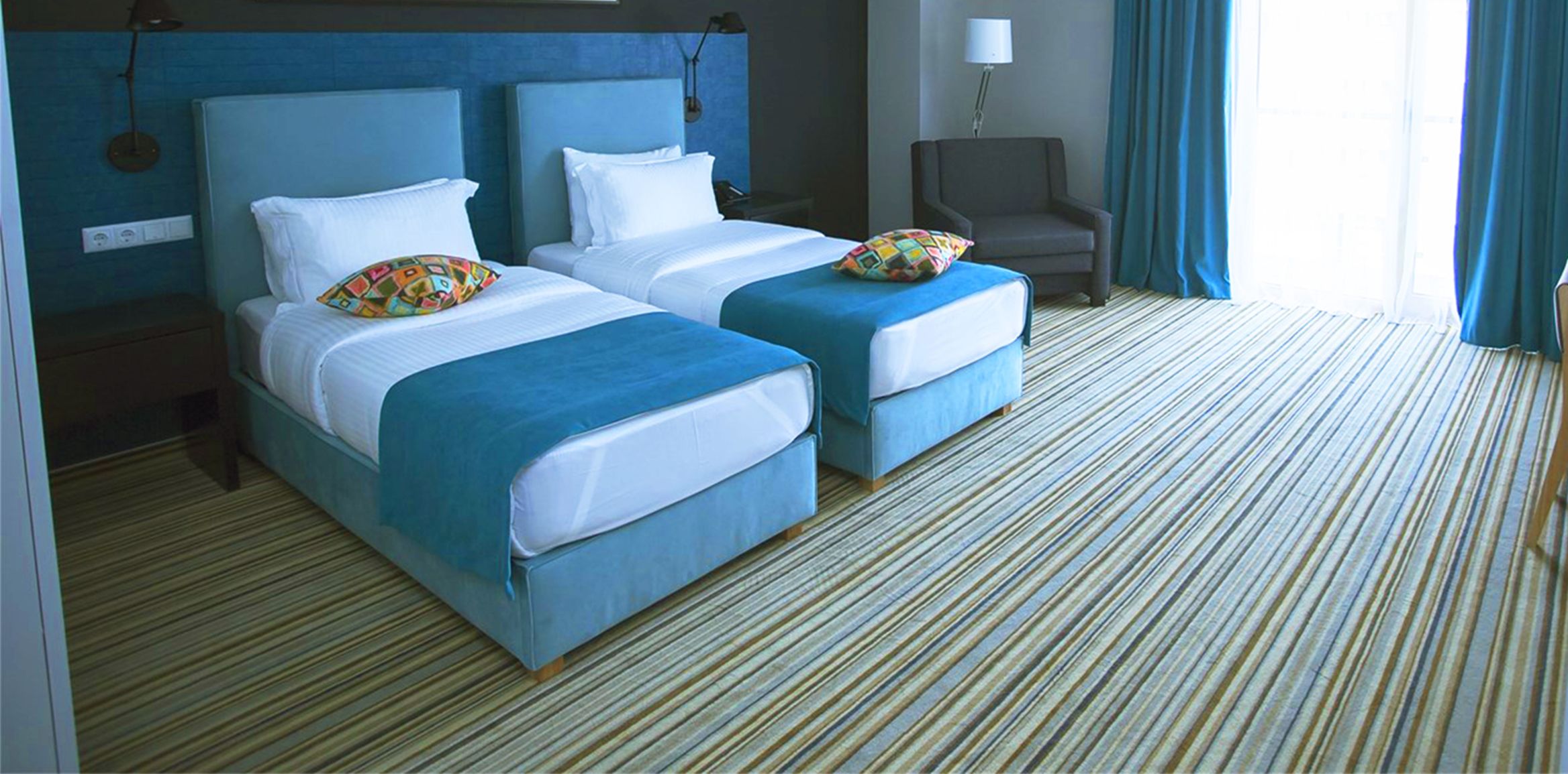 A hotel room with two beds, a chair, and a lamp.