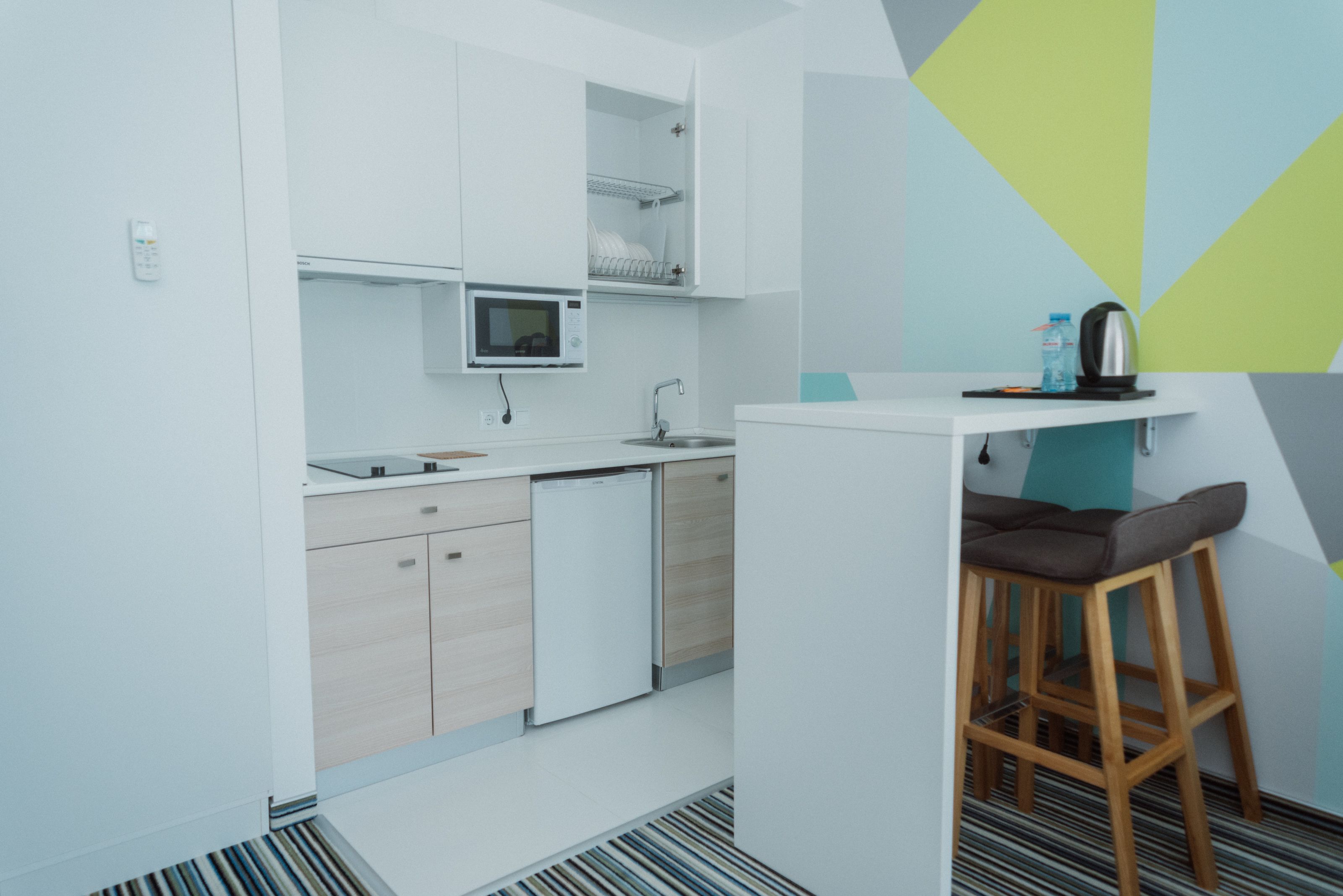 A modern kitchen with white cabinets, a microwave, a sink, and a small bar area with a stool.