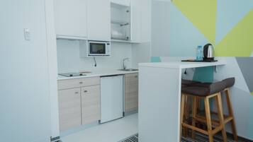 A modern kitchen with white cabinets, a microwave, a sink, and a small bar area with a stool.
