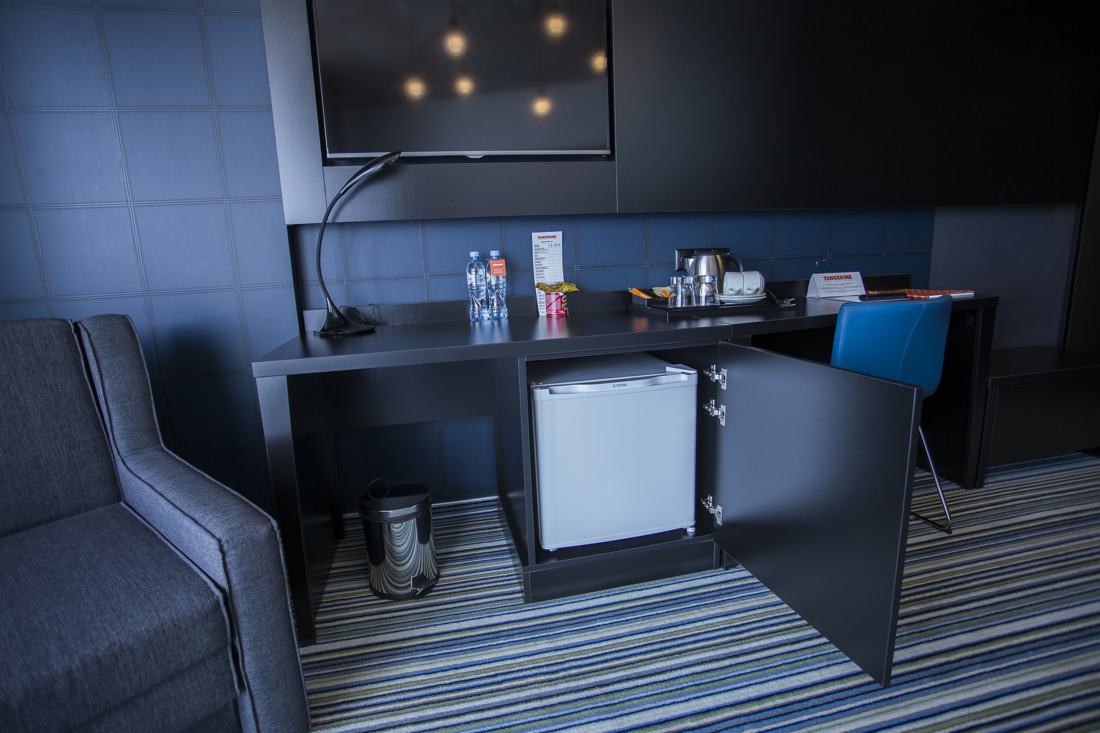 Habitación de hotel compacta con kitchenette, un televisor fijado a la pared y alfombra a rayas.