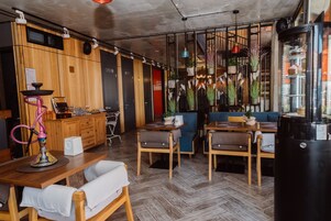 A modern cafe with wooden furniture, a bar area, and hanging plants.