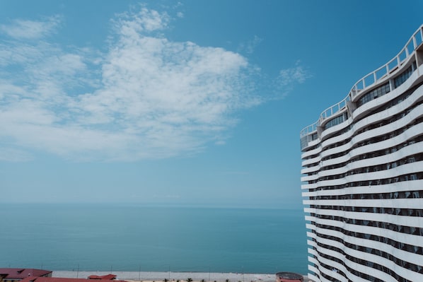 A modern hotel with a curved facade overlooking a beach and the sea.