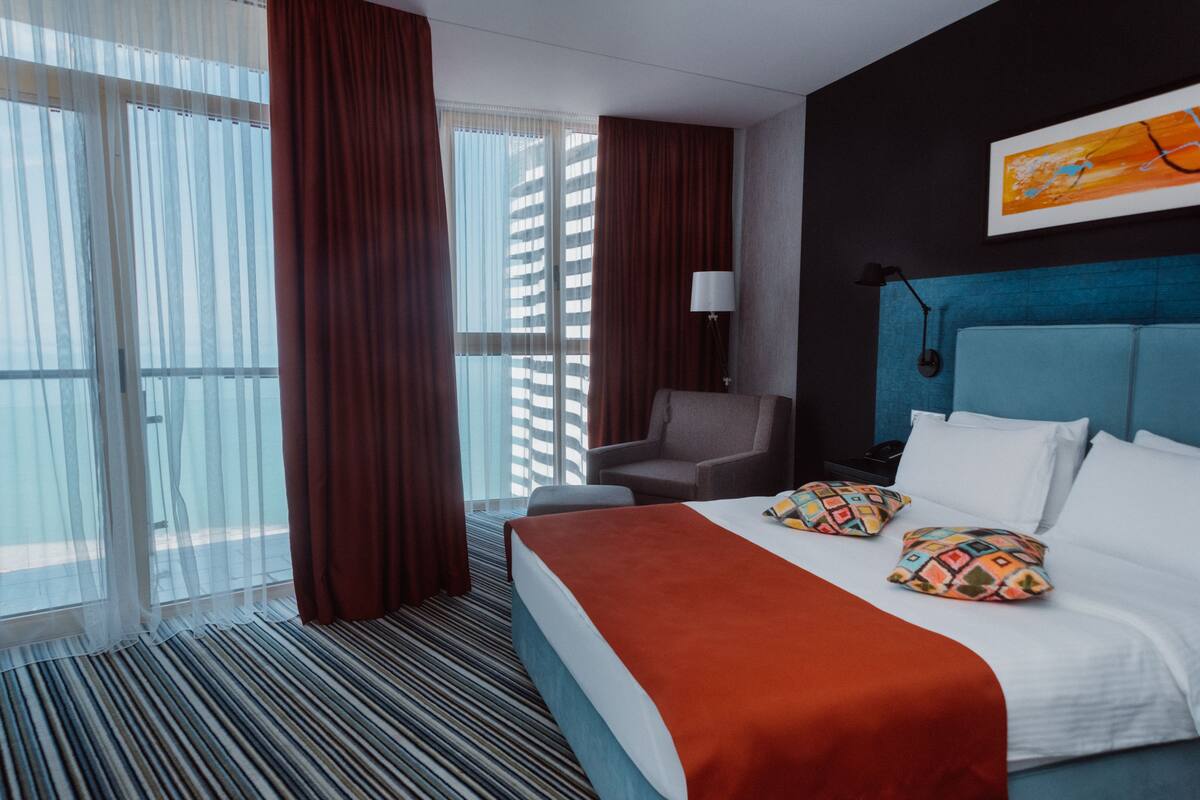 A hotel room with a large bed, a chair, a desk, and a view of the outside.