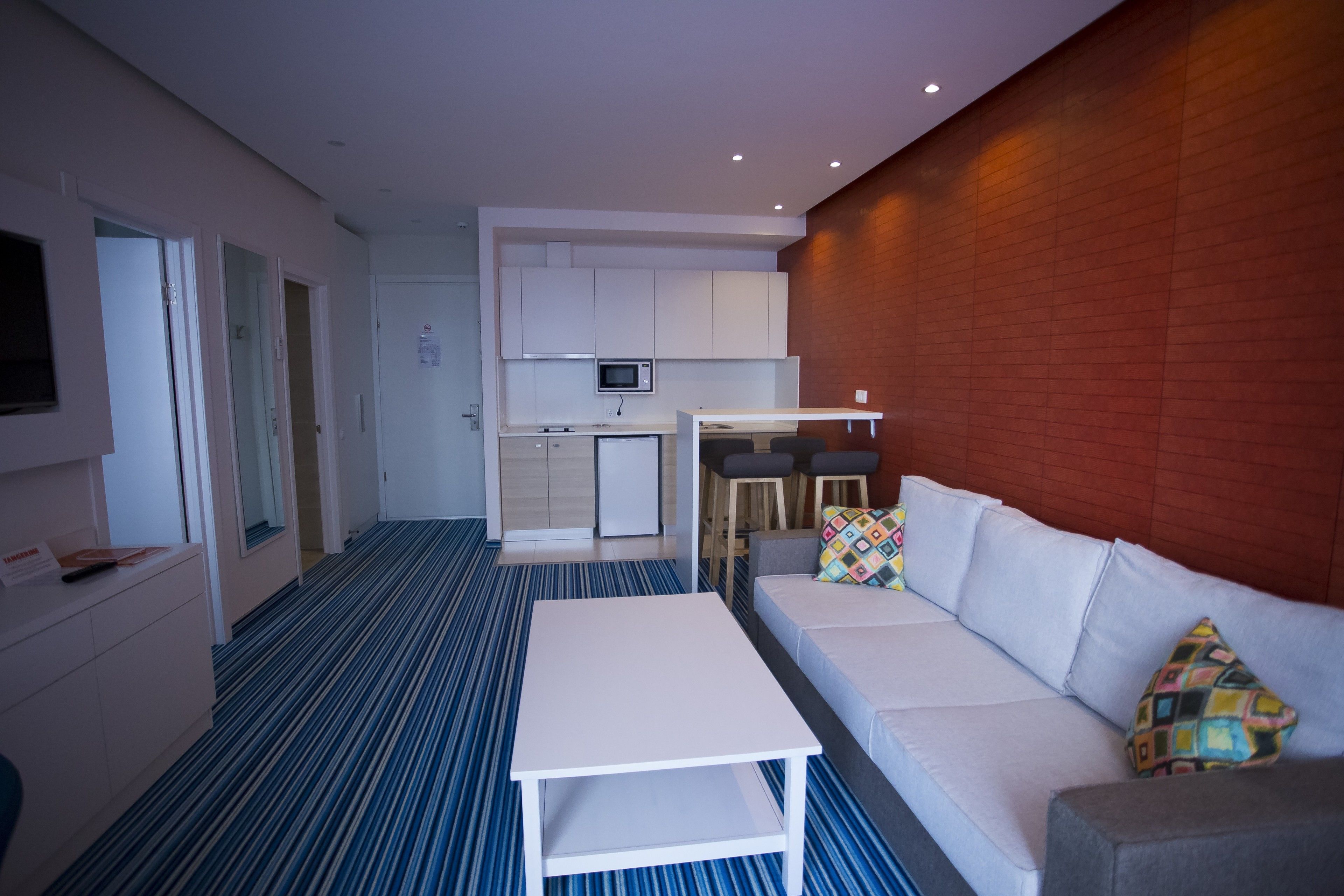 A modern hotel room with a living area, kitchenette, and a TV.