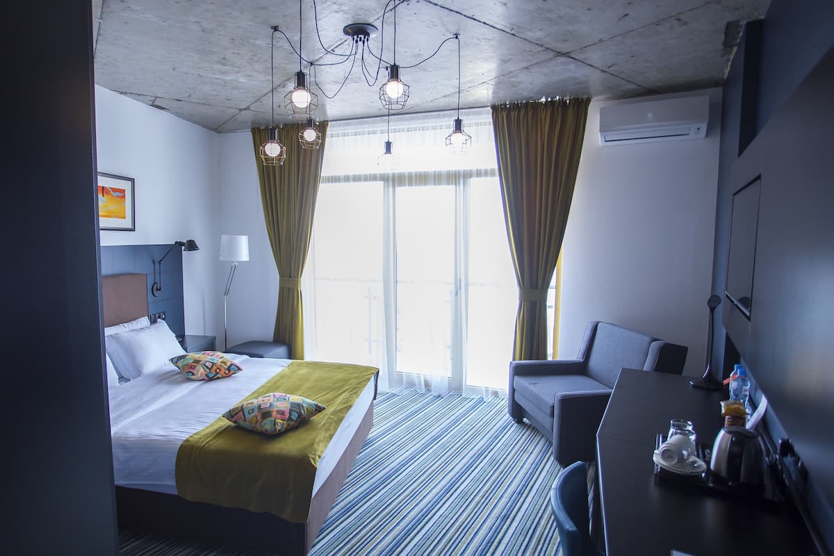 A hotel room with a bed, a desk, a chair, and a large window with curtains.