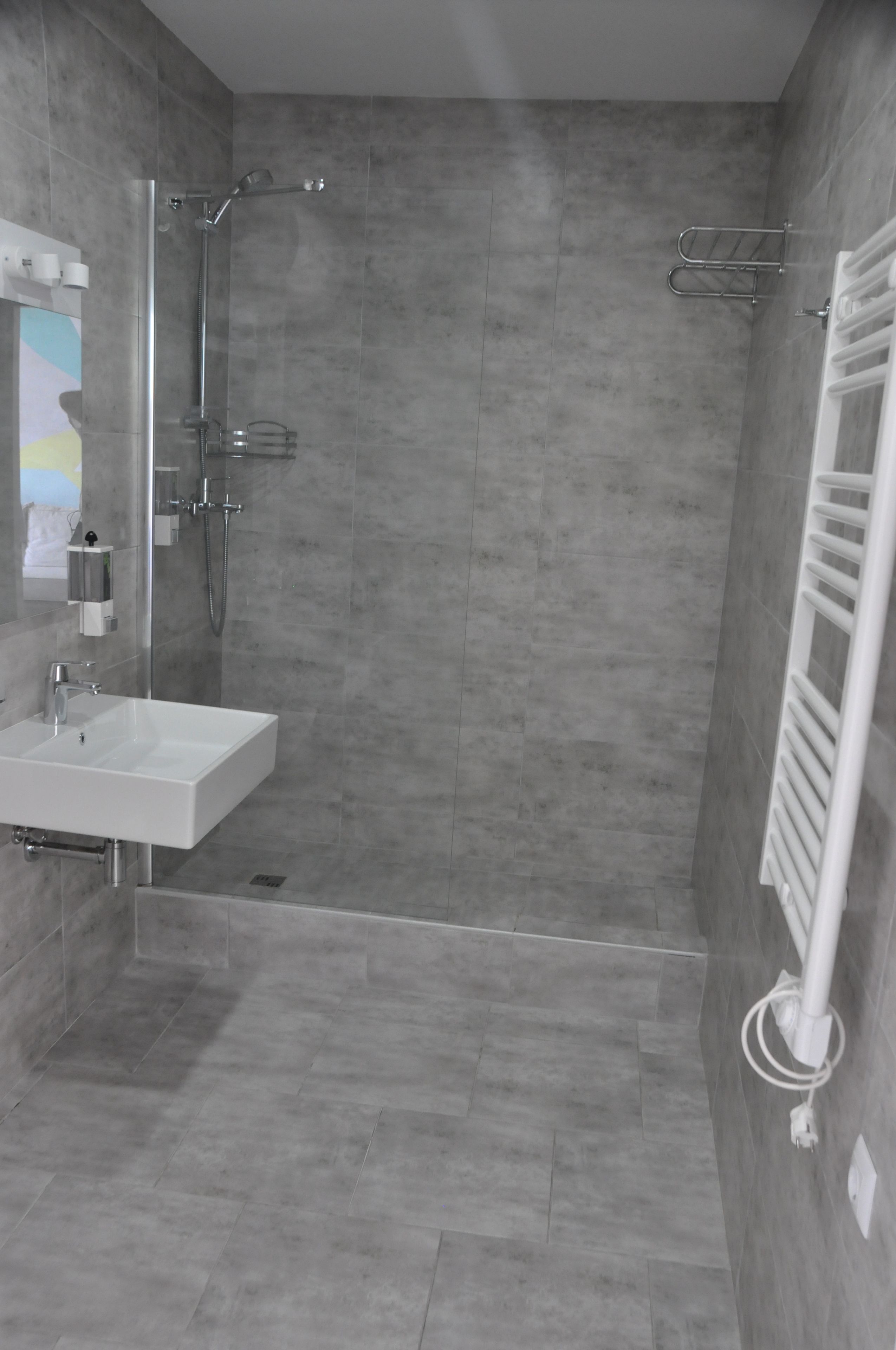 Un bagno moderno con un lavandino bianco, cabina doccia in vetro e porta asciugamani.