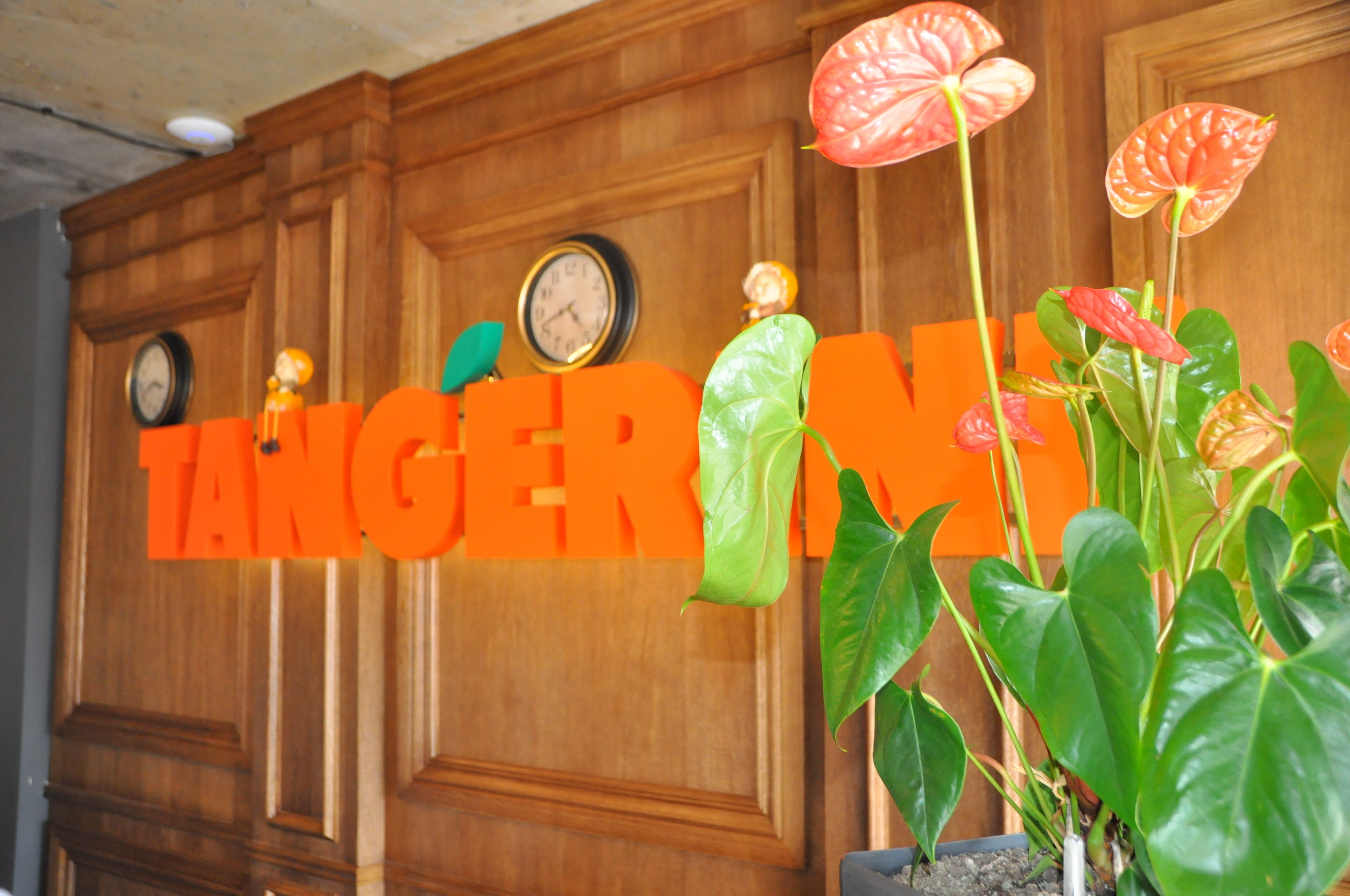 A wooden wall with clocks and a large orange sign reading "TANGERINE."