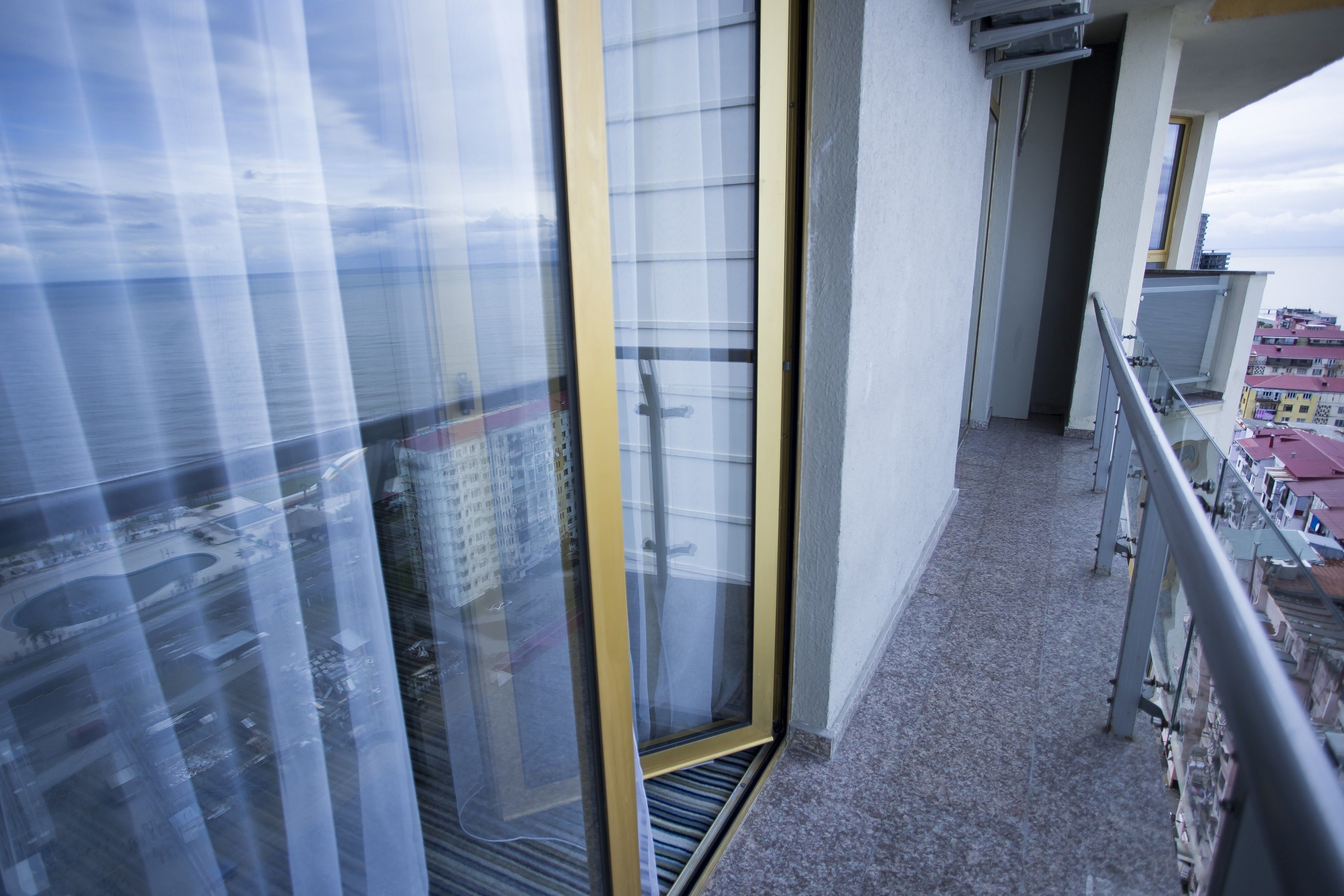 Un balcón con vistas a la ciudad, una puerta de vidrio y una barandilla de metal.