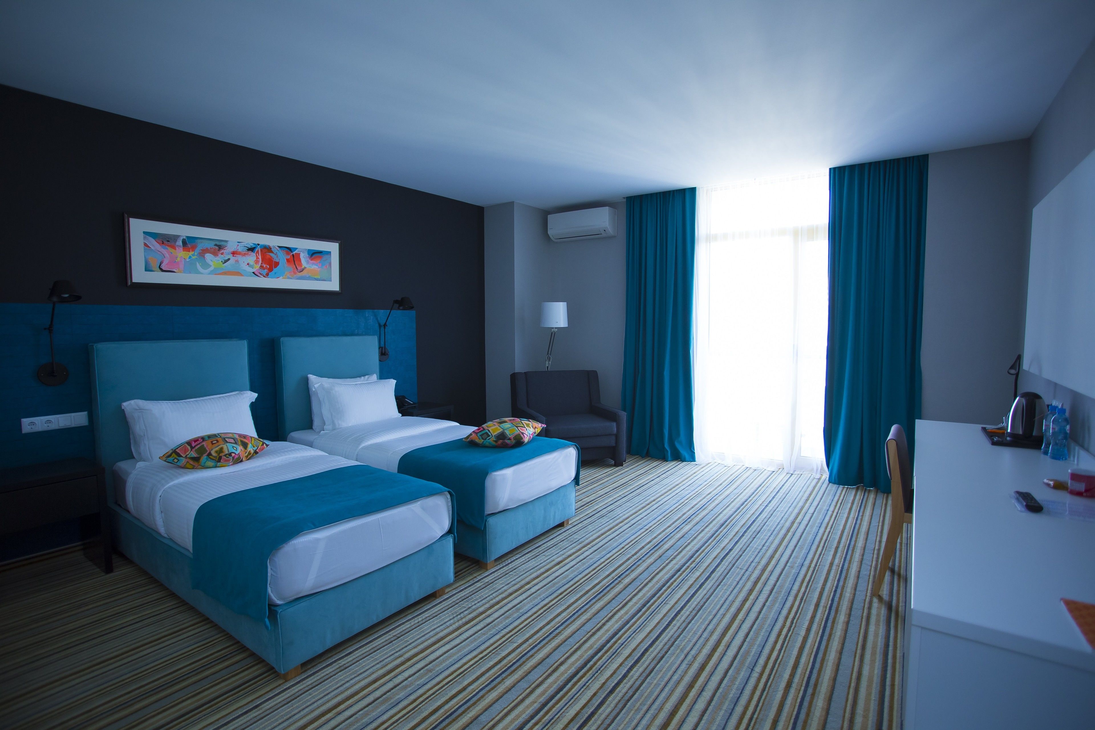 Una habitación de hotel con dos camas, un escritorio, una silla, una lámpara y un cuadro en la pared.