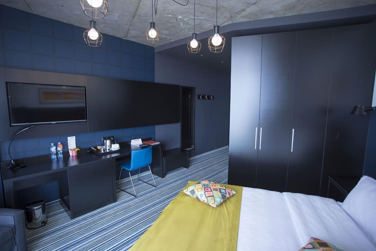 A modern hotel room with a bed, a desk, a chair, a TV, and a wardrobe.