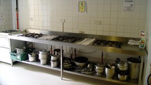 Une cuisine équipée de plusieurs cuisinières à gaz, d’appareils électroménagers en acier inoxydable et d’une variété de casseroles et de poêles rangées sur des étagères.