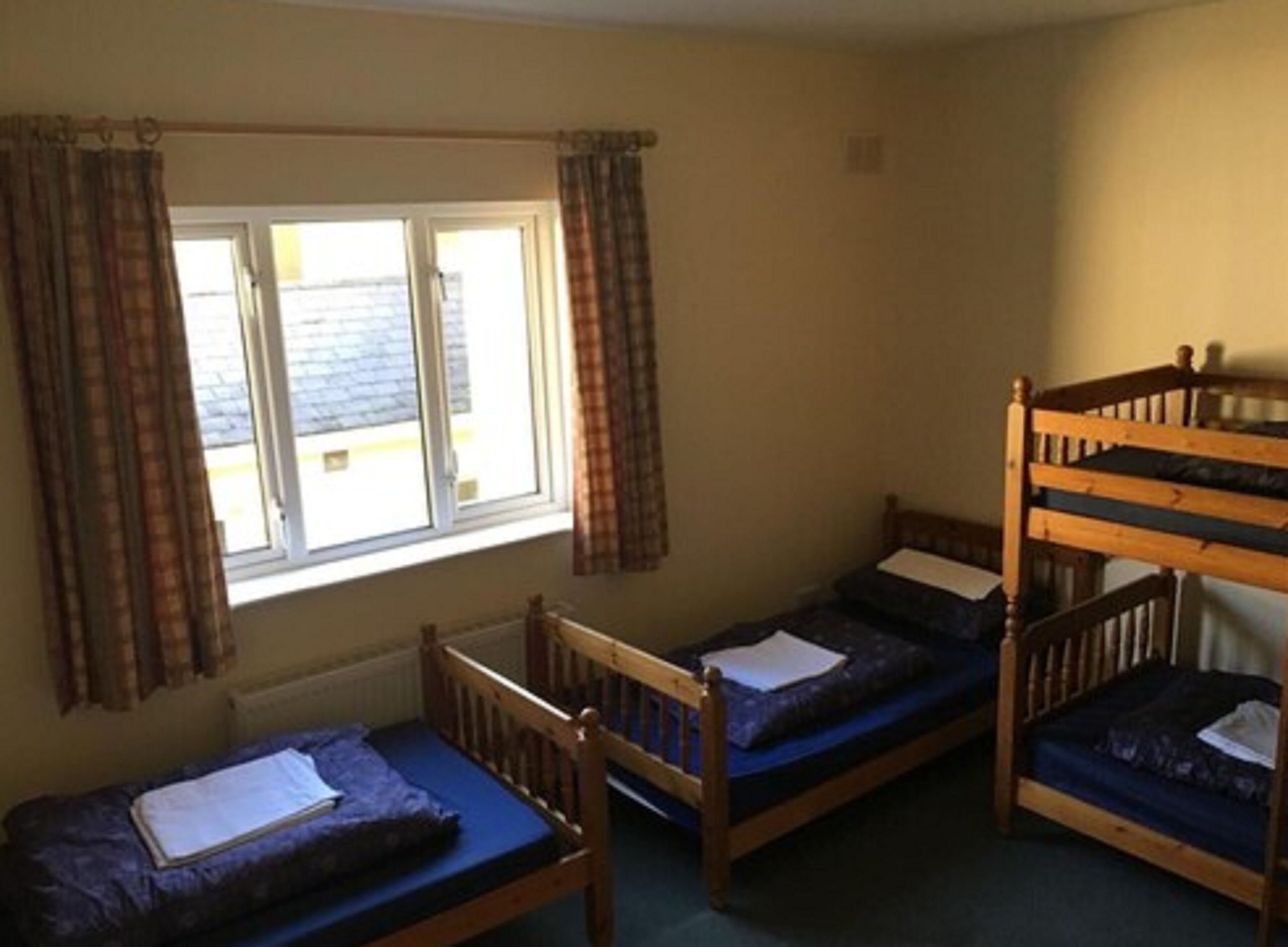 A dormitory room with two bunk beds and a single bed, a window with curtains, and a radiator on the wall.