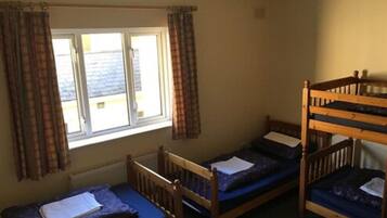 A dormitory room with two bunk beds and a single bed, a window with curtains, and a radiator on the wall.