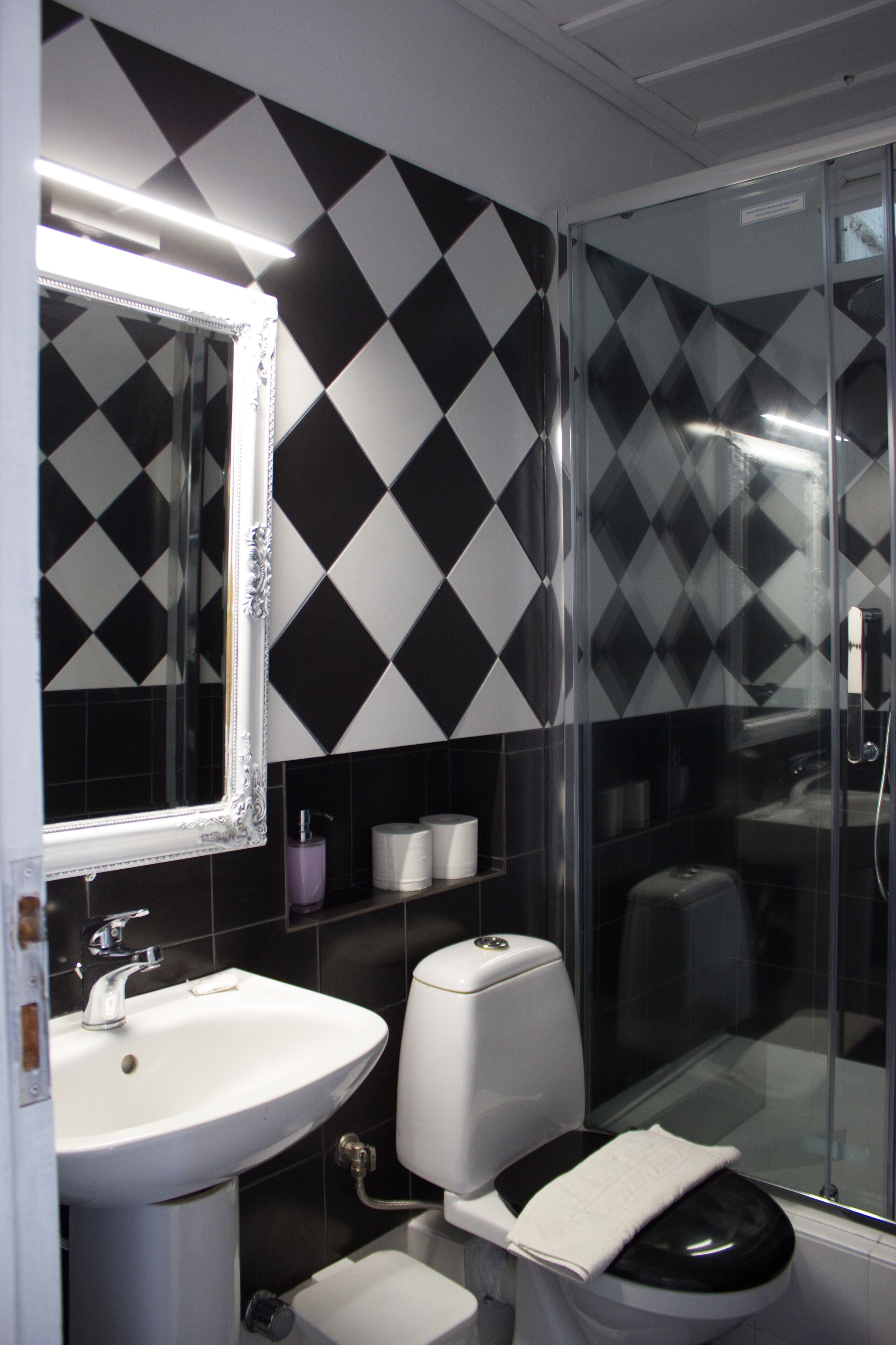 A bathroom with a black and white diamond-patterned wall, a white sink, a toilet, and a glass shower enclosure.