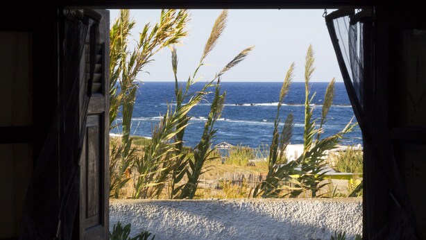 Vista a través de una ventana abierta, con una playa y el océano al fondo.