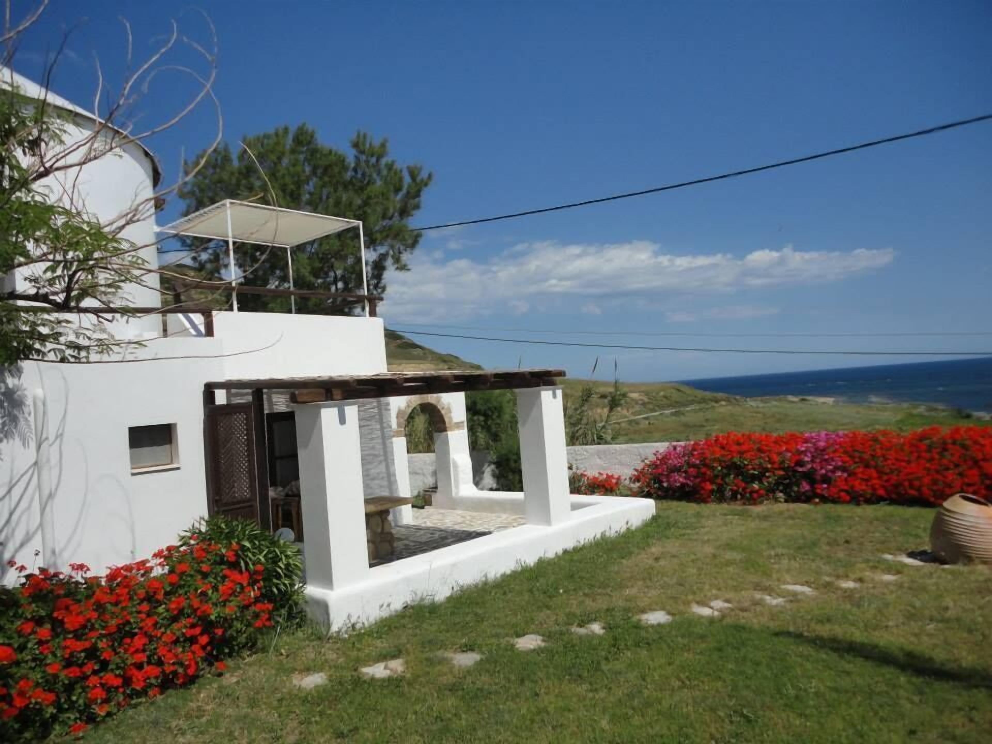 A white building with a covered outdoor seating area and a view of the sea.