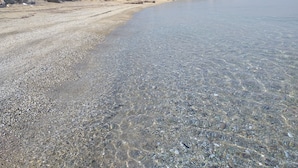 Una playa de adoquines con agua cristalina, una colina distante y una obra en construcción.