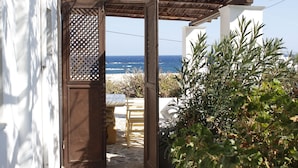 Un acceso a un patio con vista al mar, un edificio blanco y algo de vegetación.