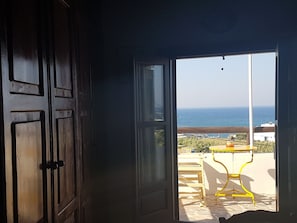 Puerta abierta que da a un balcón con vistas al mar y una silla amarilla.