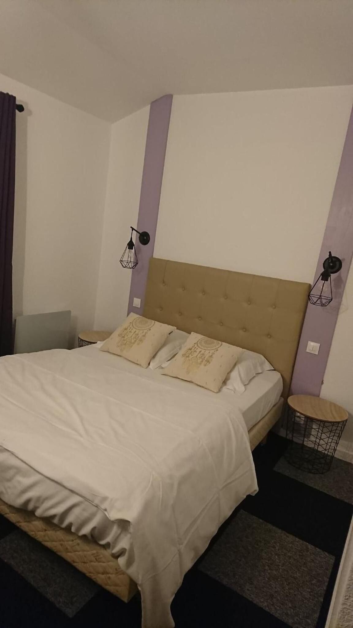Un lit bien fait, avec une tête de lit, une petite table d’appoint ronde et une lampe fixée au mur.