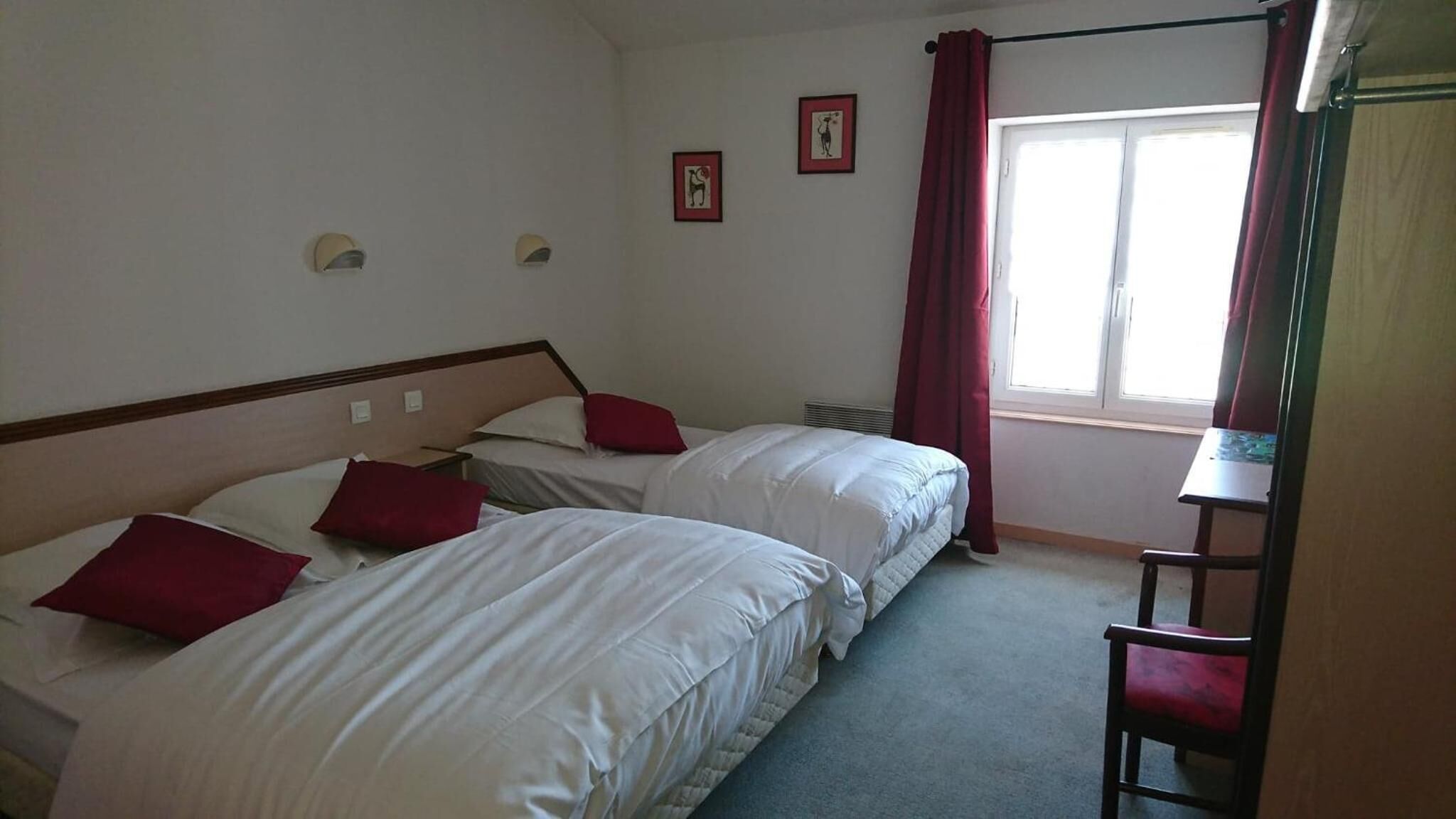 Habitación de hotel con dos camas, un escritorio y una ventana con cortinas.