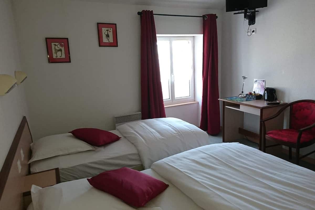 A hotel room with two beds, a desk with a chair, a TV mounted on the wall, and a window with red curtains.