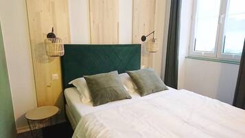Una cama con cabecera verde, dos almohadas y dos lámparas fijadas a la pared.