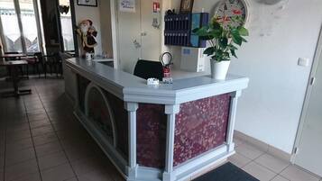 Una mesa de recepción con un reloj, una planta en maceta y un extintor.