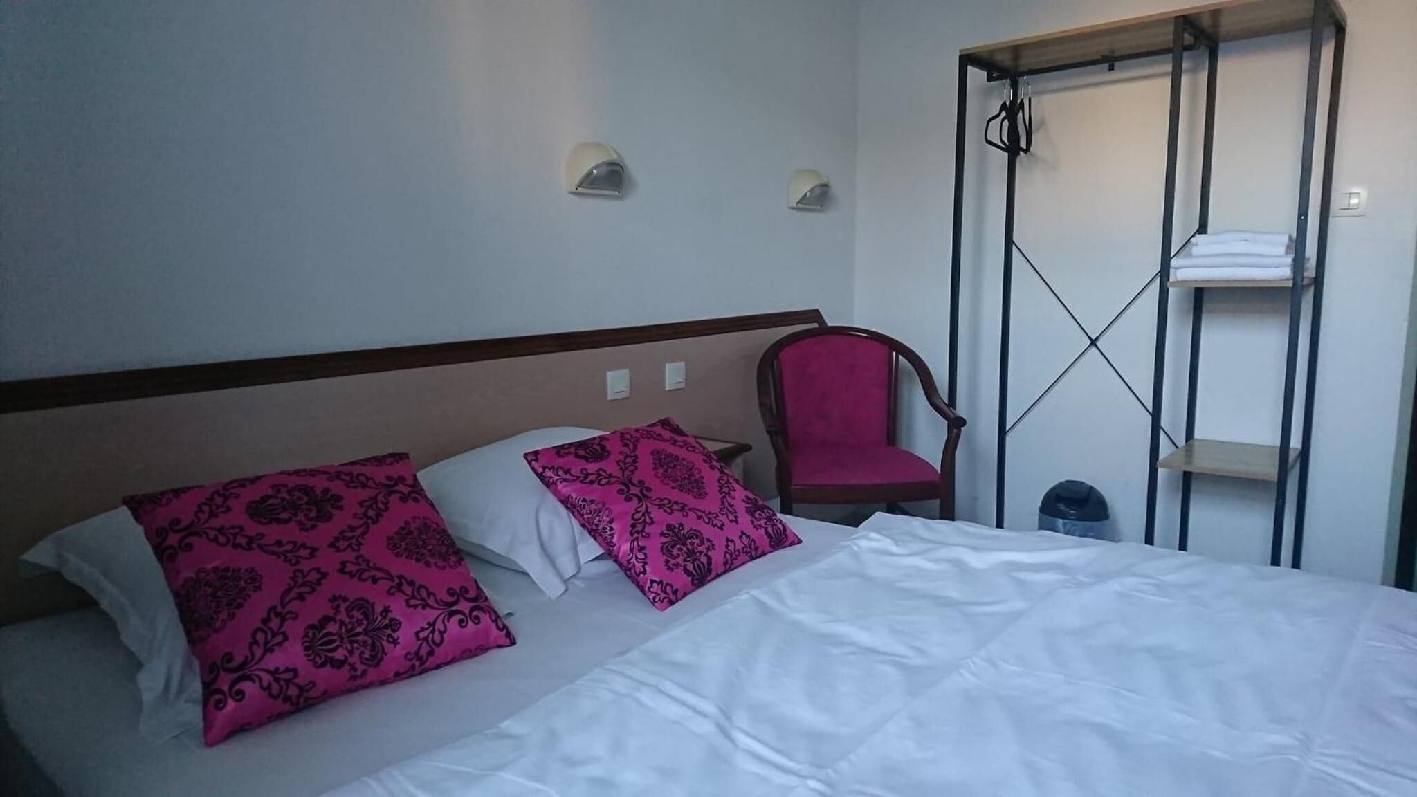 Une chambre d’hôtel comprenant un lit, deux oreillers, une chaise, une armoire et une étagère.