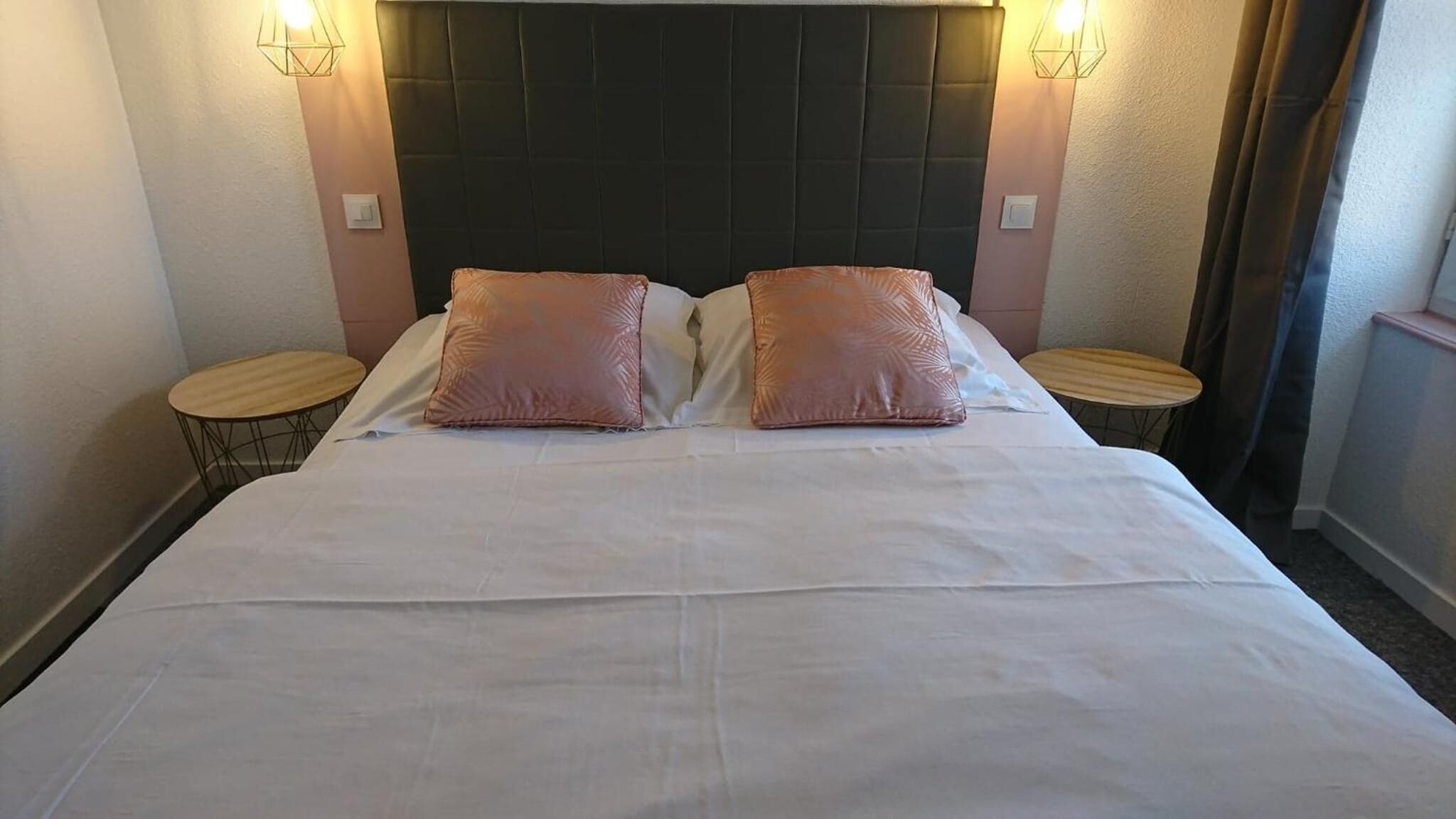Une chambre d’hôtel avec un grand lit, deux tables de chevet et des lampes fixées au mur.