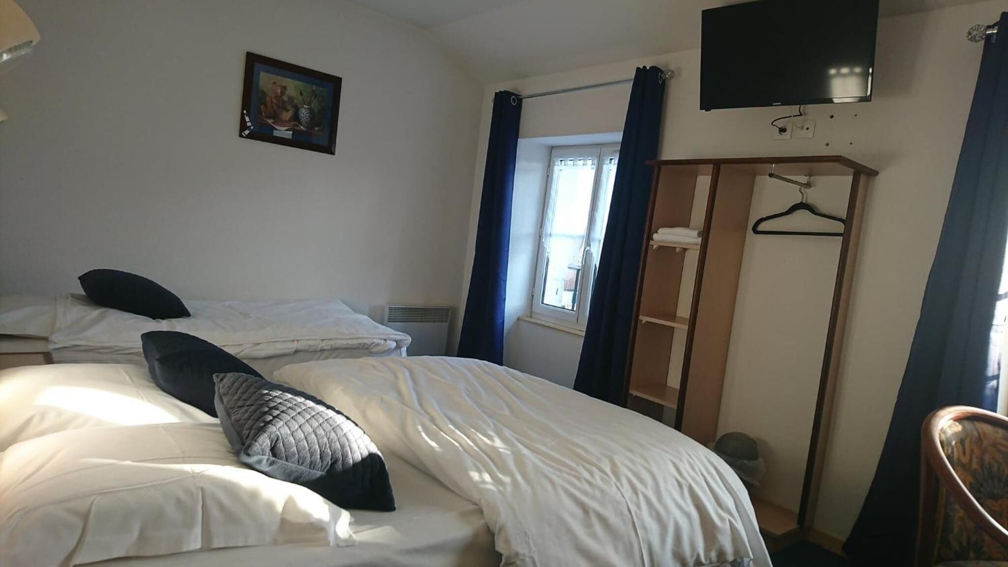 A hotel room with a bed, a wardrobe, a television, and a window with curtains.
