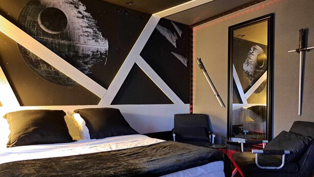 Habitación de hotel moderna con una cama grande, un escritorio y una silla. Se observa una pared con un mural de temática espacial.