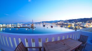 A waterfront view from a balcony with a table and chairs, boats docked in the marina, and a cityscape in the background. - The Loft Mykonos Town (Mykonos)