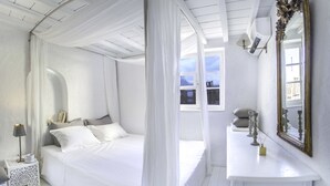 A white bedroom with a canopy bed, a bedside table with a lamp, a mirror, and a window with a view. - The Loft Mykonos Town (Mykonos)