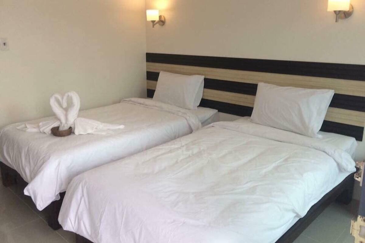 A hotel room with two beds, each with white linens and pillows. There are wall-mounted light fixtures on either side of the beds.