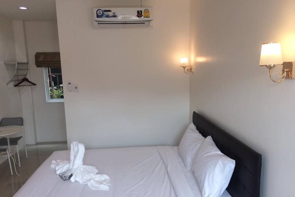 A hotel room with a neatly made bed, a wall-mounted air conditioner, and two wall sconces.