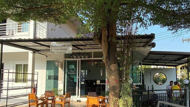 An outdoor seating area with wooden tables and chairs, a covered patio, and a signboard with contact information. - ThanaVill Resort (Mae Sot)