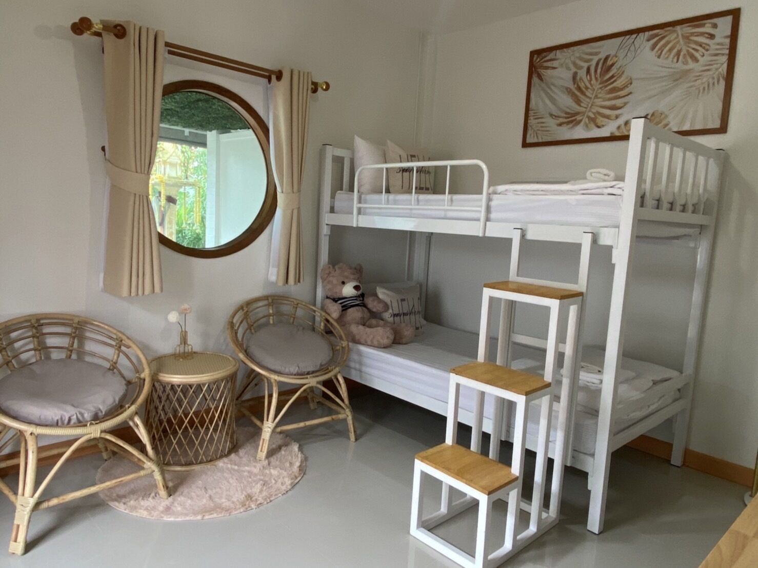 A bunk bed room with a window, a mirror, a teddy bear, and two wicker chairs.