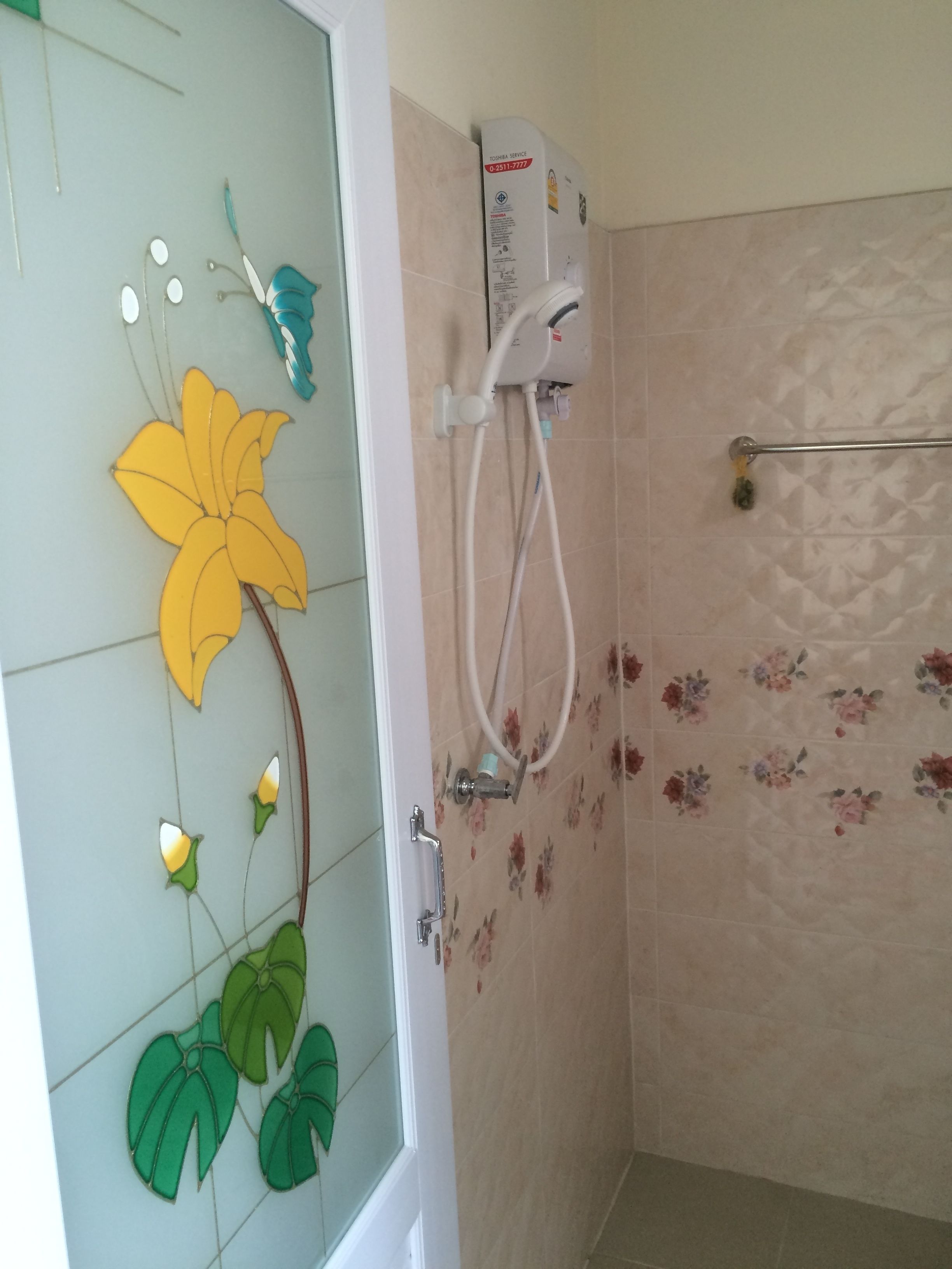 Une salle de bain équipée d’une douche, de toilettes et d’une porte en verre ornée de motifs floraux.