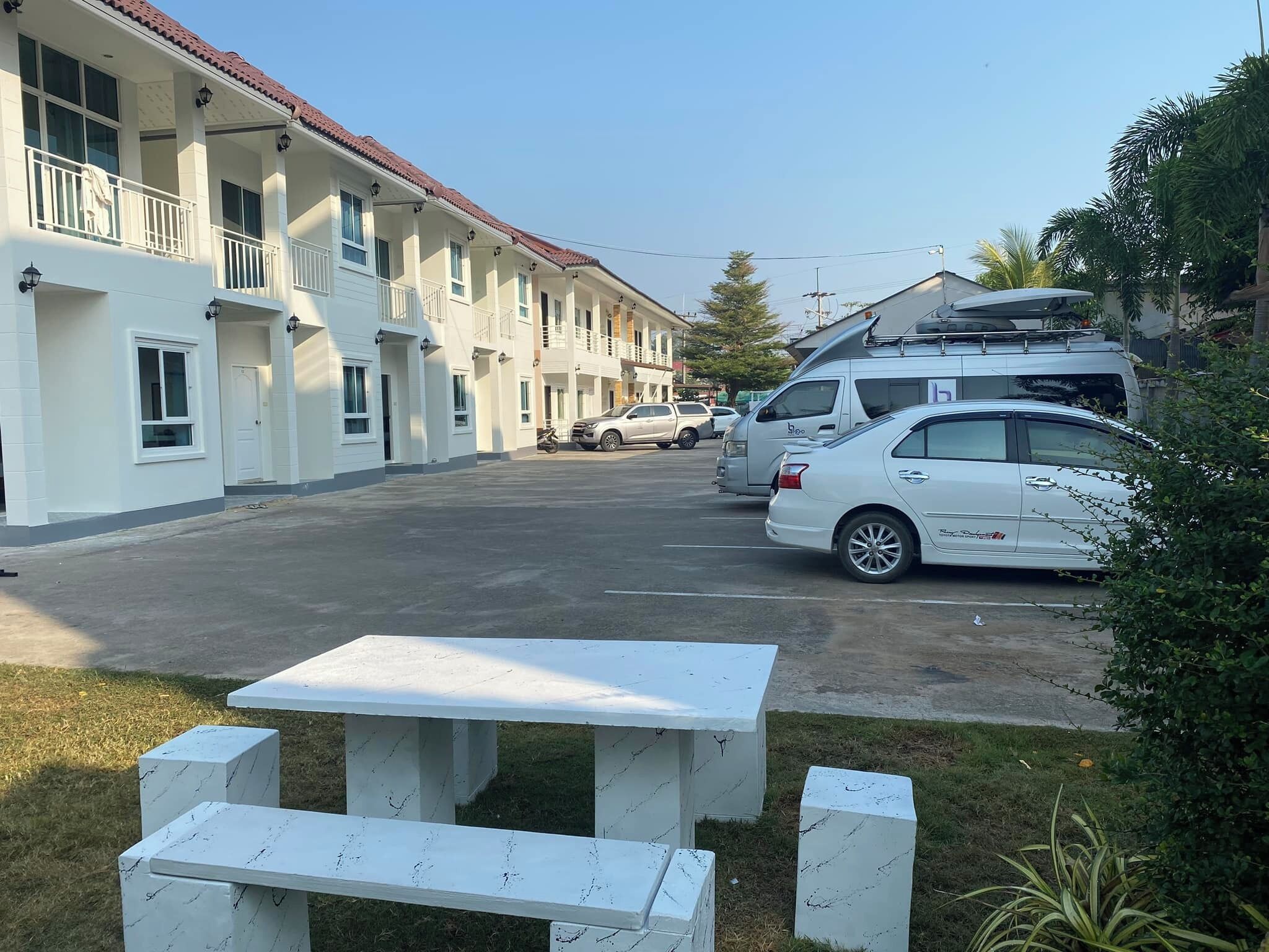 A row of white buildings with balconies, a parking area, and a picnic table.