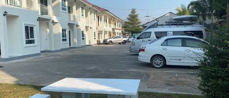 A row of white buildings with balconies, a parking area, and a picnic table.
