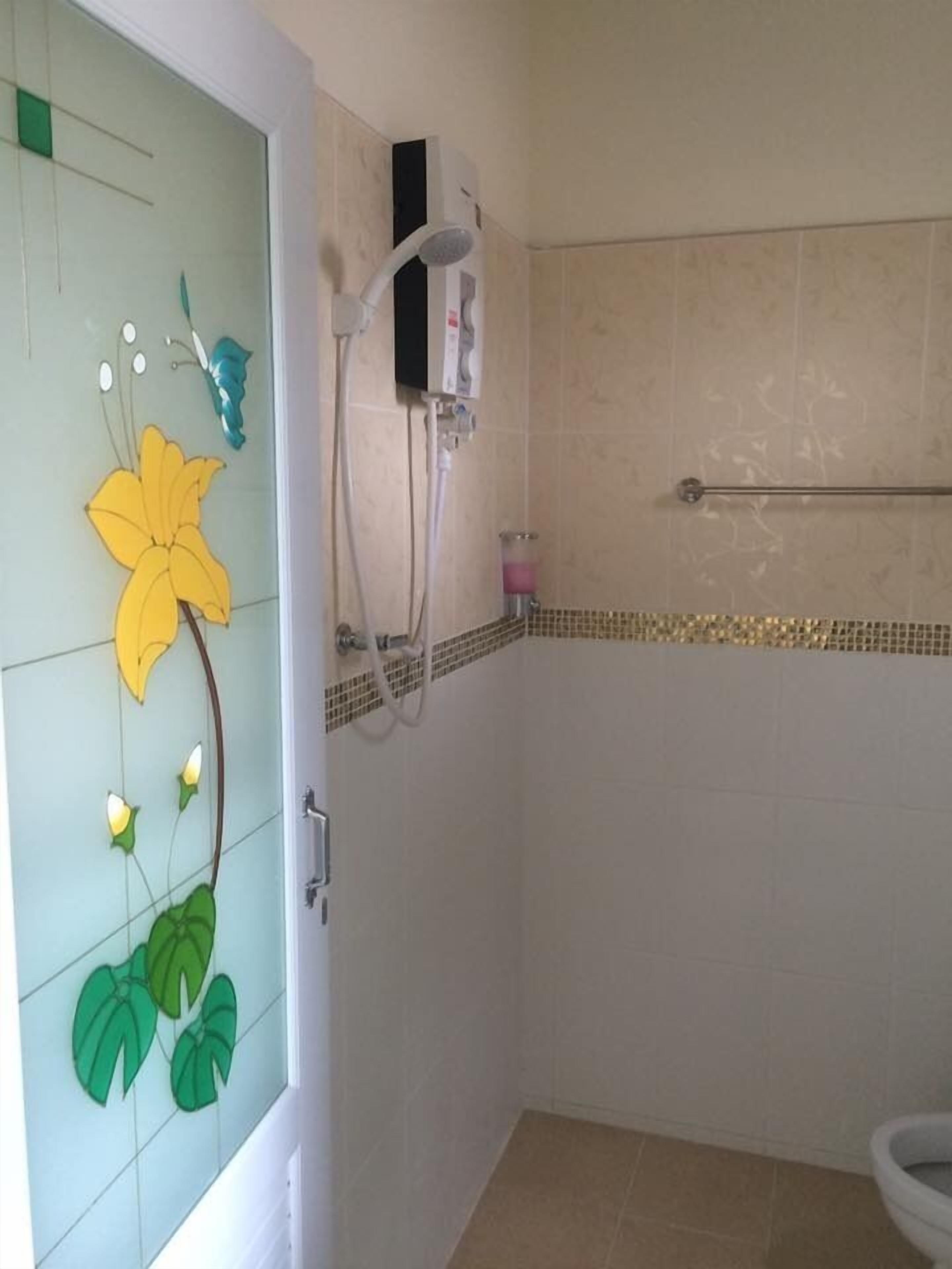 A bathroom with a glass door featuring a floral design, a shower with a handheld showerhead, and a toilet.