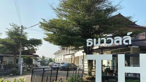 A sign with Thai characters, a gated entrance, and a building with a tiled roof. - ThanaVill Resort (Mae Sot)