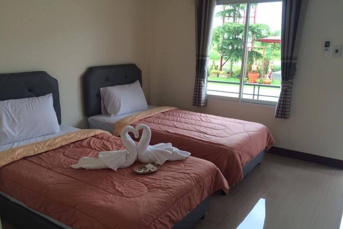 A hotel room with two beds, each with a pink bedspread and white pillows. There are two swan-shaped towels on the bed in the foreground.
