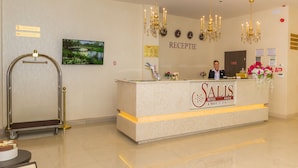 Ein Hotelrezeptionstresen mit Rezeptionistin, einem Schild mit der Aufschrift 'RECEPTION' und einem Schild mit der Aufschrift 'SALIS HOTEL & MEDICAL SPA'.