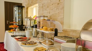 Ein reichhaltiges Buffet mit verschiedenen Speisen und Getränken, darunter Obst, Gebäck und eine Kaffeemaschine.